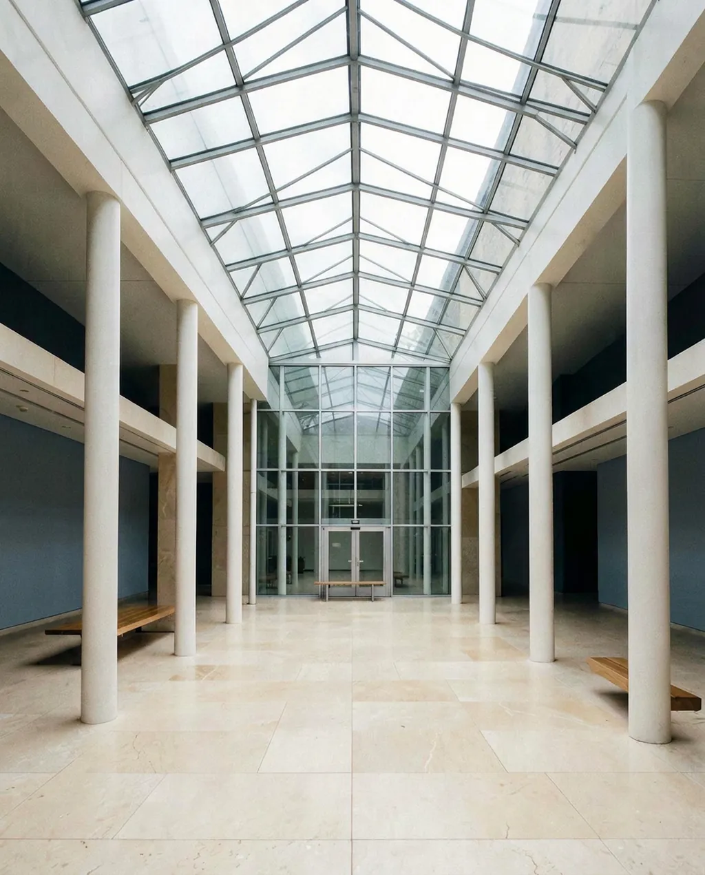 Atrium sous verrière, colonnes blanches et bancs de bois