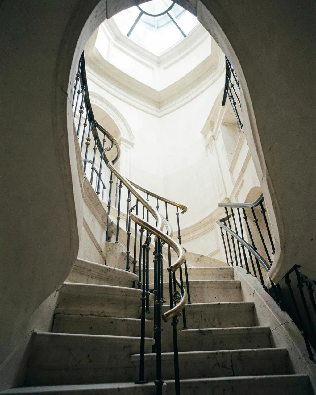 Escalier hélicoïdal en pierre claire sous une verrière