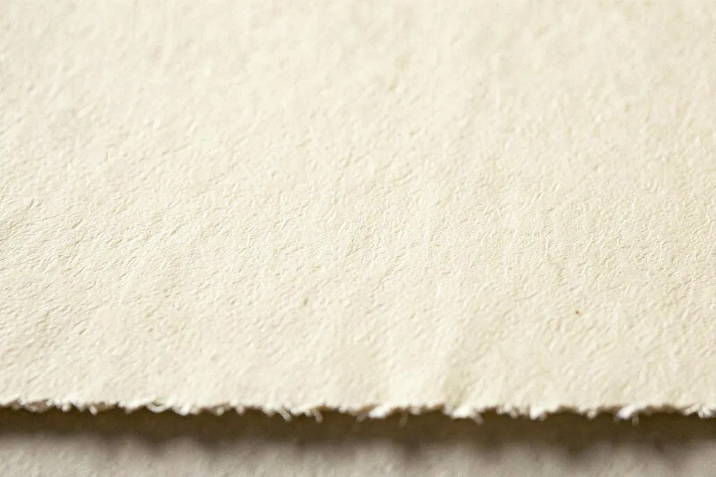 Gros plan sur un papier vergé crème, lumière rasante